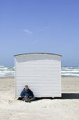 Man reads, leaning on a white bathing huts on the beach, Jutland, Denmark