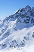 Gruppe von Skitourengehern tief unter Hoher Sonnblick mit Zittelhaus am Gipfel, Rauriser Tal, Goldberggruppe, Hohe Tauern, Salzburg, Österreich