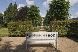 White garden bench in front of a row of trees, Borchers Garden, private garden in Goslar, Lower Saxony, Germany