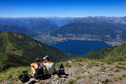 Rastende Wanderer auf dem Gipfel des Monte Tamaro, Blick zum Lago Maggiore mit Locarno und dem Mündungsdelta der Maggia, Bergwanderung zum Monte Tamaro, Tessin, Schweiz