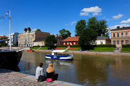 Two young women sitting on the banks of the Aurajoki river, Turku, Finland