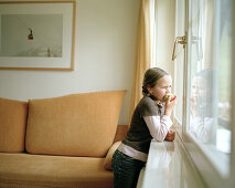 Mädchen schaut aus dem Fenster und isst einen Apfel, Zimmer, Naturhotel Chesa Valisa, Hirschegg, Kleinwalsertal, Österreich