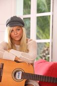 Adult, Adults, At home, Blonde, Blondes, Cap, Caps, Caucasian, Caucasians, Color, Color image, Colour, Contemporary, Daytime, Facing camera, Fair-haired, Female, Guitar, Guitars, Hat, Hats, Headgear, Hobbies, Hobby, Home, human, indoor, indoors, interior,