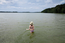 Girl wearing straw hat standing in lake Teupitz, Brandenburg, Germany