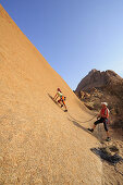 Woman climbing at red rock face, man belaying, Great Spitzkoppe, Namibia