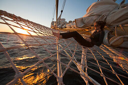 Woman relaxing in bowsprit net of sailing cruiseship Star Flyer (Star Clippers Cruises) at sunset, Pacific Ocean, near Costa Rica, Central America, America