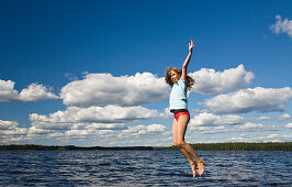 Nine year old girl jumping in the air at Boasjön lake, Smaland, South Sweden, Scandinavia, Europe