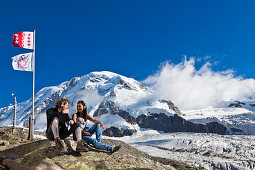 Two young people with headphones sitting on a rock, myclimate audio trail, New Monte Rosa Hut, Zermatt, Valais Alps, Canton of Valais, Switzerland