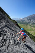 Woman climing up a rock face, valley of Sarca and mountains of Lake Garda in the background, Dro, Trentino, Italy, Europe