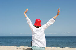 Woman wearing a red hut stretching at beach, List, Sylt, Schleswig-Holstein, Germany