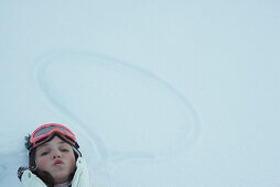 Teenage girl lying on the ground next to word bubble drawn in snow, looking at camera