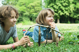 Two girls lying on grass, holding sticks, smiling, one with Down's Syndrome