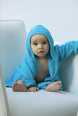 Baby wearing hooded bathrobe sitting in armchair, looking at camera, portrait