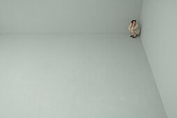 Woman crouching in corner of large empty room, holding head, high angle view