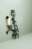 Man climbing precariously stacked chairs