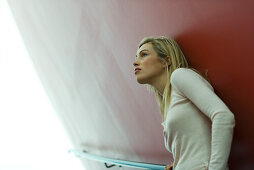 Woman leaning against wall, looking up in thought