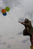 Female watching as bunch of balloons float away up into cloudy sky
