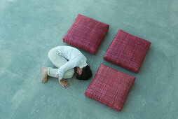 Three square cushions and man arranged in square shape, man lying in fetal position, high angle view