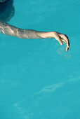 Woman floating in pool, cropped view of arm