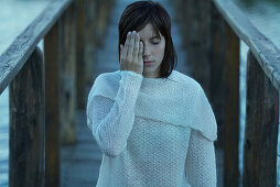 Woman covering one eye, standing on wooden pier, waist up