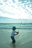 Boy throwing out fishing line on beach, rear view