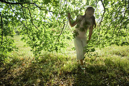 Girl walking under branches, looking up, full length