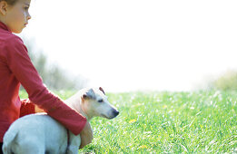 Girl sitting on grass with arm around dog