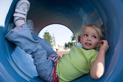 Girl lying in playground tunnel with legs up, looking away, close-up
