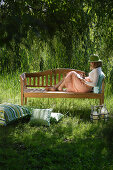 Frau sitzt mit einem Buch auf einer Gartenbank, Simssee, Bayern, Deutschland