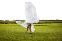 Young woman holding a white sheet, oudoors