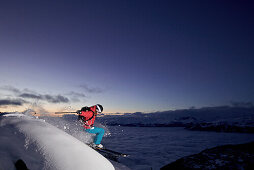 Skifahrerin springt über einen Vorsprung in der Abenddämmerung, Chandolin, Anniviers, Wallis, Schweiz