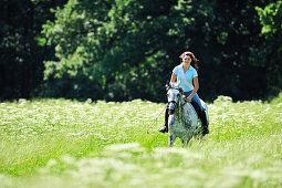 Woman riding a horse through a meadow, Inn Valley, Upper Bavaria, Bavaria, Germany