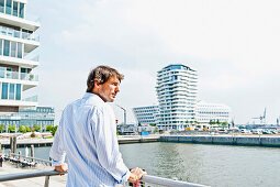 Mann mittleren Alters blickt auf Strandkai, Marco-Polo-Tower im Hintergrund, HafenCity, Hamburg, Deutschland