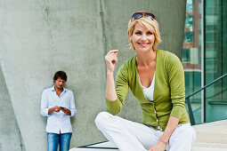 Woman sitting on step, man with mobile phone standing in background, HafenCity, Hamburg, Germany