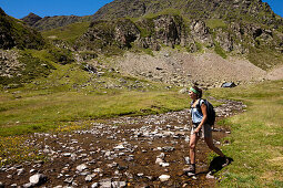 Female hiker crossing river near Lac Roumassot, Ossau Valley, French Pyrenees, Pyrenees-Atlantiques, Aquitaine, France