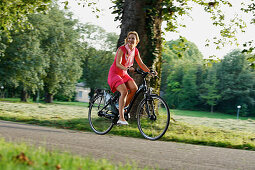 Woman cycling through Rosenstein Park on an E-Bike, bike tour, e-bike, Rosenstein Park, Stuttgart, Baden-Wurttemberg, Germany