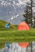 One person crouching beside a tent along a lake shore, Berner Oberland, Grosse Scheidegg, Valais, Switzerland, Europe