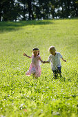 Sibling (5 and 7 years) running over a meadow, Lake Starnberg, Bavaria, Germany