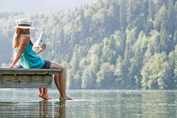 Two teenage girls sitting on a jetty at lake Schwansee, Schwangau, Allgaeu, Bavaria, Germany