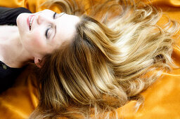 Portrait of a young woman lying, long hair on yellow textil fabric