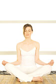 Young woman sitting cross-legged, yoga attitude, shut eyes