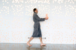 Man in grey bathrobe, walking, holding a vase, side view