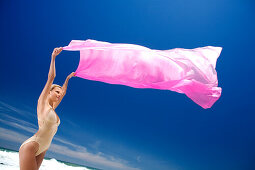Young woman in swimming costume holding pink pareo in wind