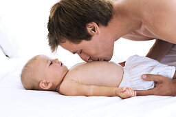 Portrait of a father kissing his baby's chest, lying on bed, indoors