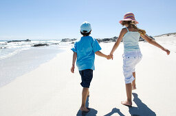 Brother and sister walking on the beach, rear view, outdoors