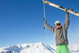 Young man holding his skis above his head