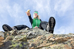 Young woman sitting on a rock in the mountains, holding a banana, See, Tyrol, Austria