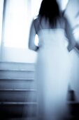 Blurry back view of a woman in a white dress walking up a stairway, indoors