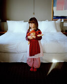 Girl with rag doll beside a hotel bed, Rotterdam, Netherlands