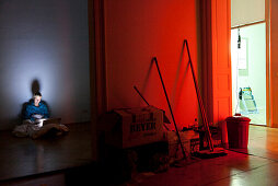 Frau sitzt auf Boden in einer leeren Wohnung, arbeitet am Laptop, Notebook, Computer, Parkett, Umzug, rotes Licht, Besen, Melancholie, MR, Leipzig, Sachsen, Deutschland